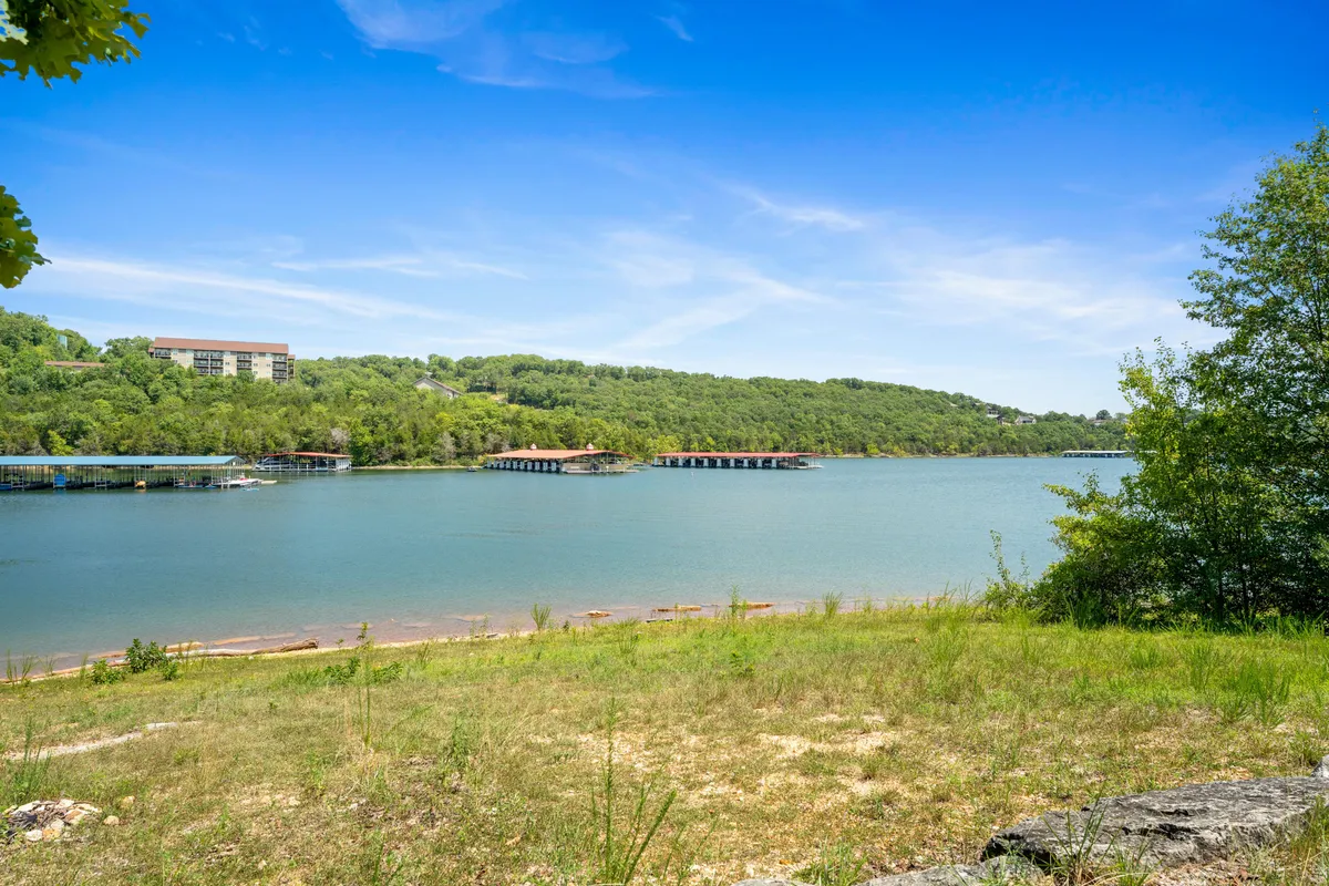 A tranquil lake is surrounded by rolling green hills and a spacious sky overhead. Boathouses dot the shoreline, and the calm water reflects the colors of the sunset. The serene setting is ideal for leisurely walks, quiet moments on the shore, and enjoying nature together.