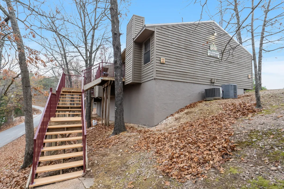 A tranquil exterior featuring a staircase, the building's exterior, and mature trees in the background. The scene emphasizes the connection between accommodations and the surrounding Ozark nature.