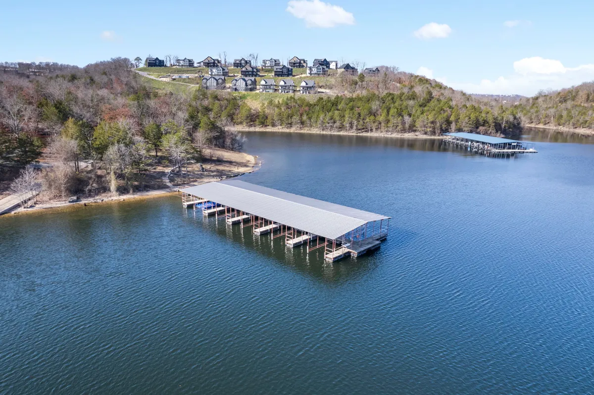 A peaceful lakeside dock surrounded by water and houses set against a lush, green hillside. The setting is quiet and natural, ideal for strolls or nature walks with your pet, with open spaces inviting exploration and relaxation.