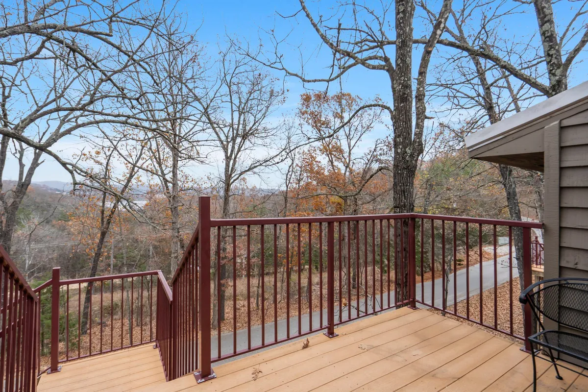 A wooden deck with a sleek metal railing overlooks a canopy of trees and a distant landscape. The scene is peaceful and inviting, suggesting a private space to relax, enjoy nature, or stargaze in the evening.