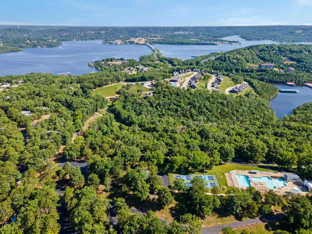 An expansive view over the resort’s landscape, showcasing lush greenery, a swimming pool, tennis courts, a lake, and residential buildings. The image captures the breadth of outdoor amenities and a sense of space and freedom for family activities.