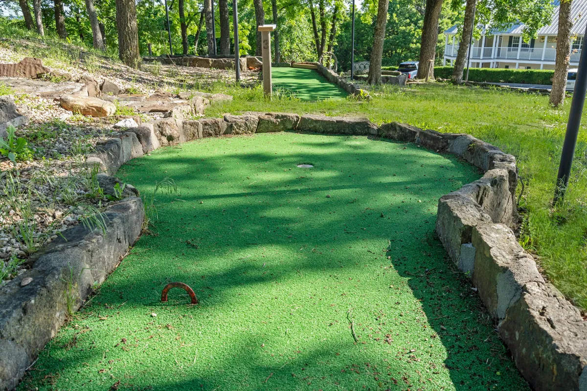 A vibrant exterior scene featuring a winding mini-golf pathway surrounded by lush greenery and natural stone borders. Families and children are visible, enjoying a lively game of mini-golf in a relaxed, joyful atmosphere. Benches and trees provide a welcoming, shaded setting.