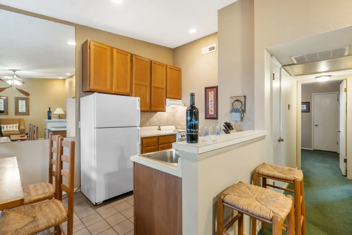 A bright, fully equipped kitchen with an island and bar stools, ample cabinetry, and a refrigerator. The space feels ready for shared cooking, lively conversation, and entertaining guests.
