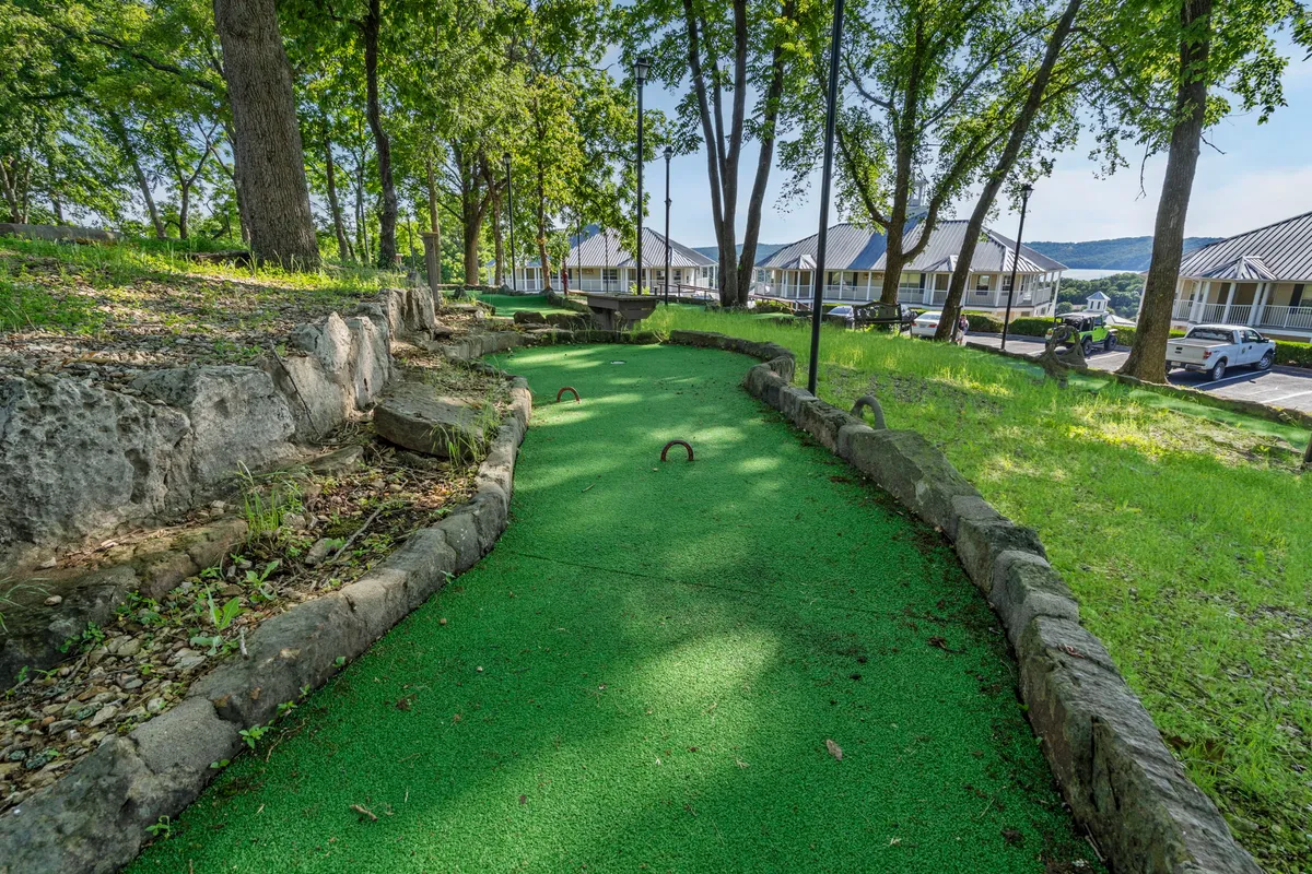 An inviting exterior shot of a mini-golf course bordered by natural stone and surrounded by lush greenery. The area is open and playful, blending recreational activity with the peacefulness of the outdoors.